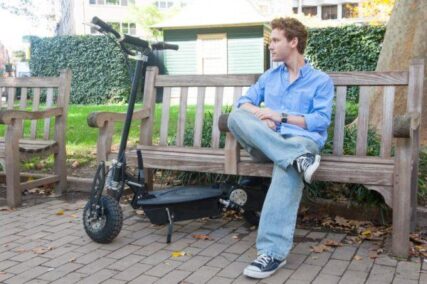 A young man sitting on a bench with the Urban 1000-watt 36v LITHIUM Electric Scooter